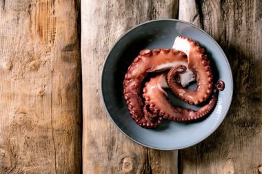 Coocked tentacles of octopus on blue ceramic plate over brown wooden background. Top view, flat lay. Copy space