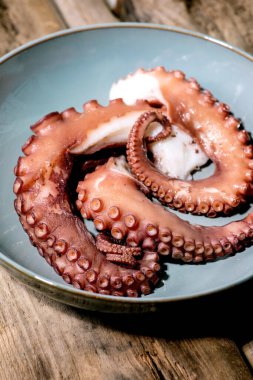 Coocked tentacles of octopus on blue ceramic plate over brown wooden background. Close up