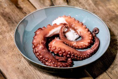 Coocked tentacles of octopus on blue ceramic plate over brown wooden background