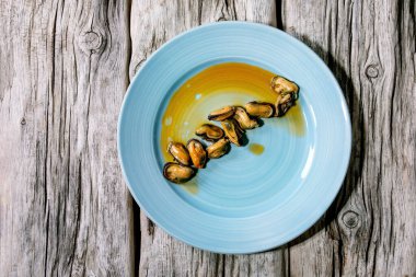 Smoked mussels in oil on blue ceramic plate over old grey wooden background. Top view, flat lay. Copy space