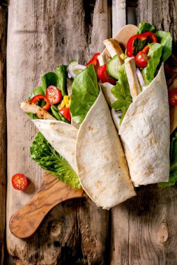 Traditional mexican tortila wrap with pork meat and vegetables on wooden cutting board over brown wooden background. Top view, flat lay. Homemade fast food