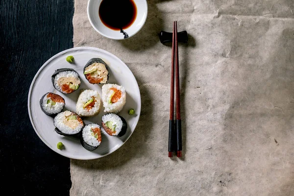 自制寿司卷 配上鲑鱼 日本煎蛋卷 芥末和酱油 灰色纸上的筷子盖在黑色木制背景上 日本风格的晚餐 — 图库照片