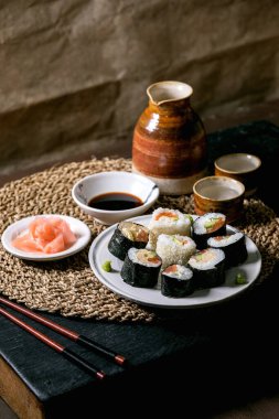 Somon balığı, Japon omleti, avakado, zencefil ve soya soslu ev yapımı suşi ruloları. Çubuklu çubuklar saman peçetenin üzerinde. Seramik içecek sake seti. Japon usulü akşam yemeği