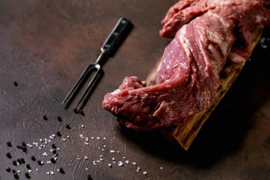 Ahşap tahtada taze çiğ sığır filetosu eti metal et çatalı, tuz ve biber ile koyu kahverengi doku arka planında. Yemek pişirme konsepti. Yaklaş, kopyala samanı.