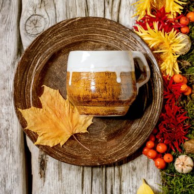 Sonbahar tatili sofrası. Boş zanaat seramik tabağı ve sonbahar meyveleri, yosun ve çiçeklerle süslenmiş eski ahşap masa kupası. Düz konum, kopyalama alanı. Kare