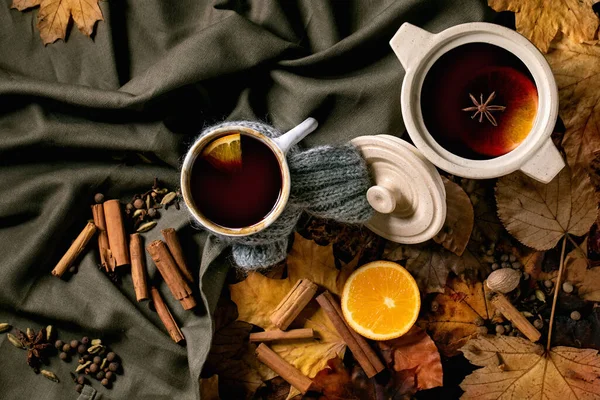 将热的覆酒放入瓷壶中 并在深色亚麻布桌布上用围巾 橙子和秋天的叶子盛在杯子里 平躺在床上舒适温暖的酒精饮料 平躺在床上 — 图库照片