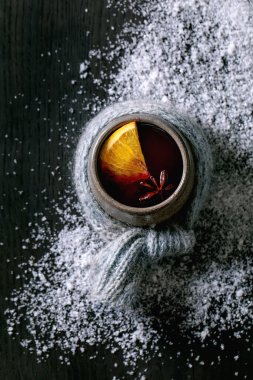 Sıcak sıcak şarap seramik bardakta baharatlı ve portakal dilimli siyah ahşap arka planda kar eşarplı. Düz yat, boşluğu kopyala