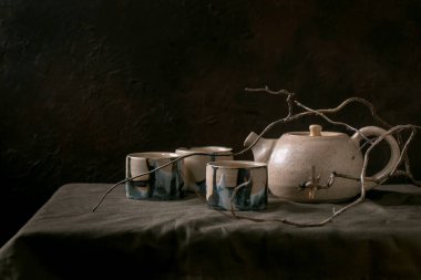 El yapımı beyaz benekli çaydanlık. Çay seremonisi için bir fincan sıcak yeşil çaydanlık. Karanlık odada keten masa örtüsünün üzerinde duruyor..