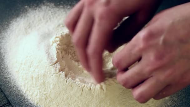 Женские руки разбивают яйцо на муку для приготовления теста на черном столе — стоковое видео