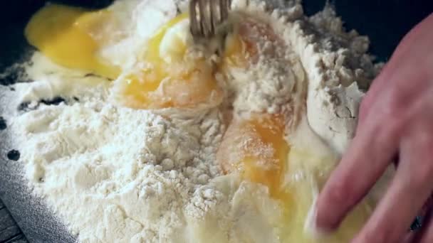 Las manos femeninas amasan los huevos en harina para hacer masa sobre la mesa negra — Vídeo de stock