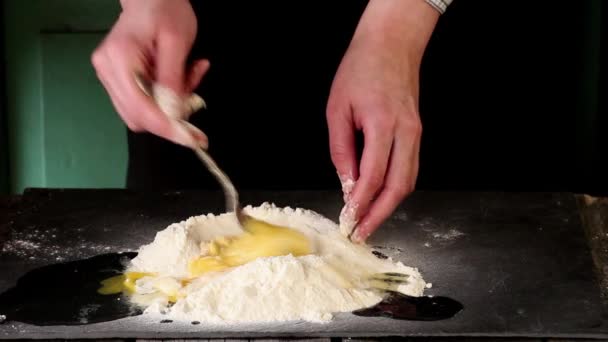 Женские руки месят яйца в муке для приготовления теста на черном столе — стоковое видео