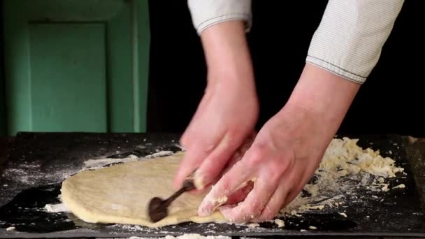 Mains féminines tranchant la pâte pour pâtes par rouleau vintage sur la table noire, poudrant par la farine — Video