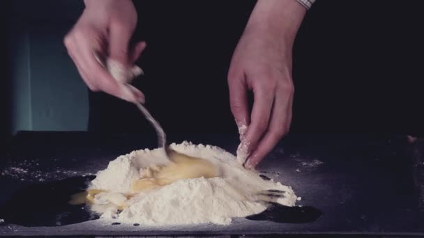 女性の手は、黒いテーブルの上の生地を作るための小麦粉に卵をこねます。暗いの素朴なスタイル。レトロなフィルター効果で — ストック動画