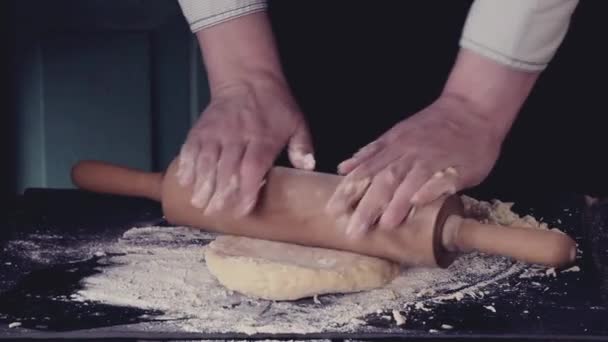 Mains féminines déroulant la pâte pour pâtes par rouleau à pâtisserie en bois sur une table de cuisine noire, pulvérisant par farine. Style rustique sombre. Effet filtre rétro — Video
