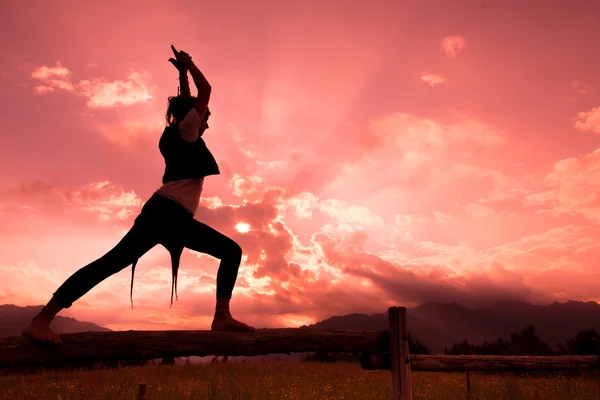 Meisje op hek in de natuur met rode sky maakt Turnen yoga movem — Stockfoto