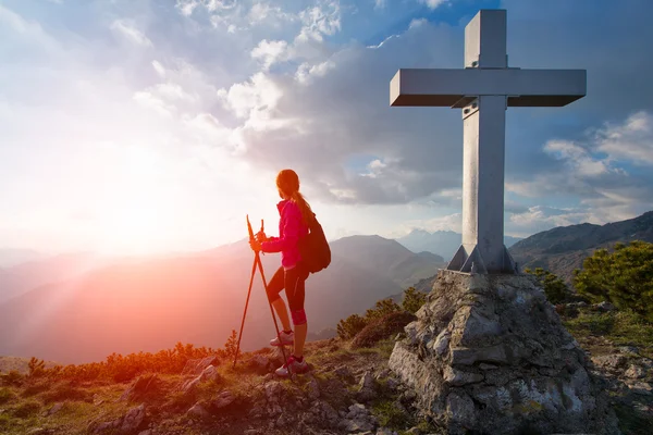 Mulher observa o pôr do sol do topo de uma montanha com cruz — Fotografia de Stock