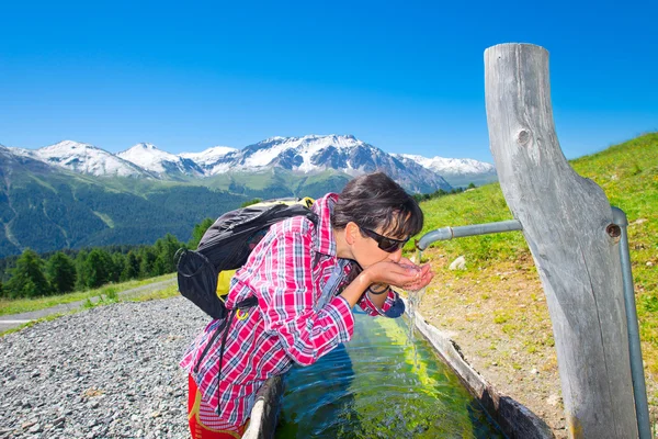 Flicka hiker släcker törst vid fontänen under en mountain tre — Stockfoto