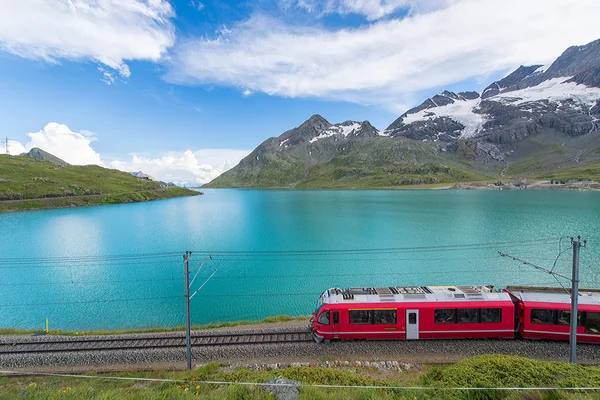 Röda tåget i de höga bergen i de schweiziska Alperna passerar nära ett — Stockfoto