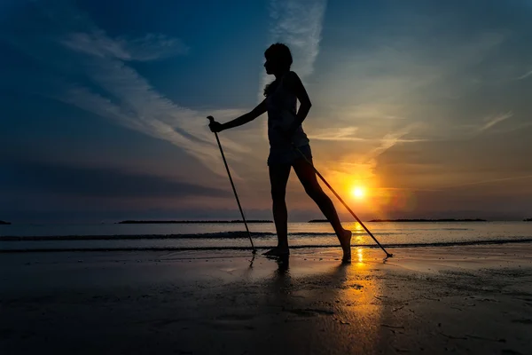 Skinny dívka při východu slunce na pláži u moře s Nordic walki — Stock fotografie