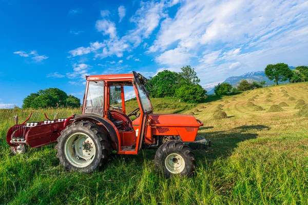 Trator vermelho em um prado de montanha com fardos de feno feitos à mão — Fotografia de Stock