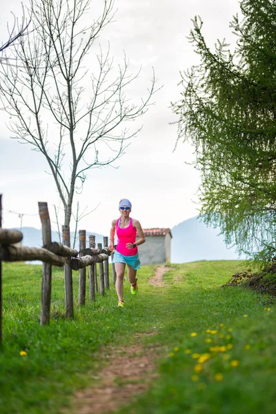 Chica rubia atleta corre un camino de montaña en la hierba verde — Foto de Stock