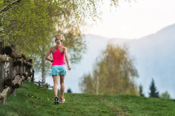 Chica rubia atleta corre un camino de montaña en la hierba verde — Foto de Stock