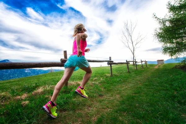 Chica rubia atleta corre un camino de montaña en la hierba verde — Foto de Stock