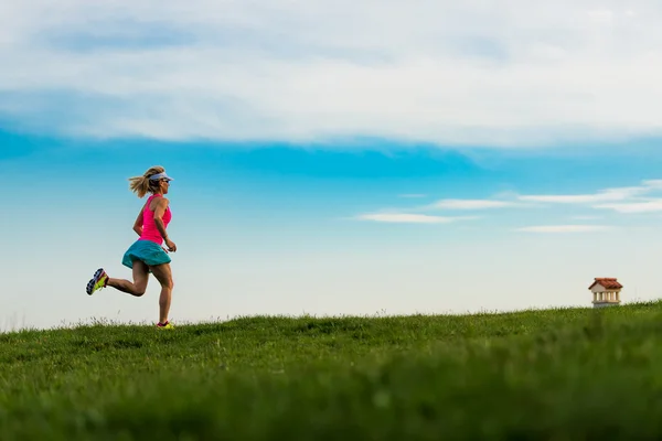 Blondynka zawodnik biegnie w zielony łąka w górach — Zdjęcie stockowe