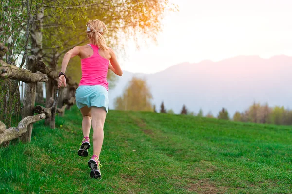 Bionda atleta ragazza corre un sentiero di montagna nell'erba verde — Foto Stock