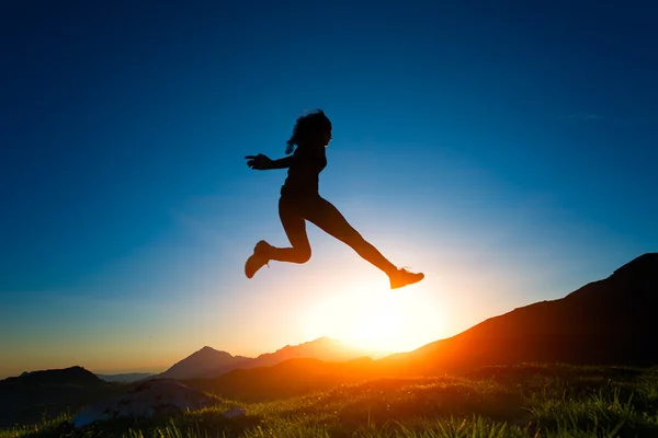 Chica salta durante una puesta de sol en las montañas — Foto de Stock