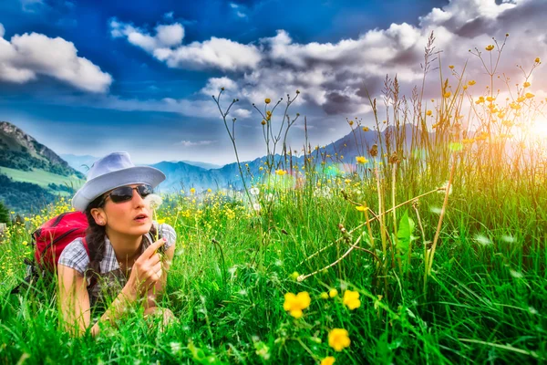 Girl in mountain meadow blowing flower — Stock Photo, Image