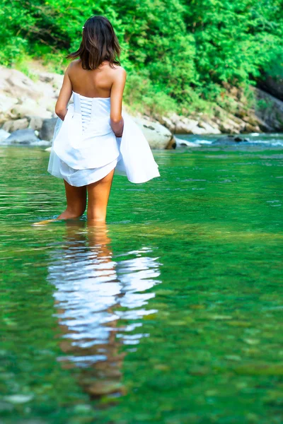 Young, beautiful and lonely bride It gets wet legs in a river. — Stock Photo, Image