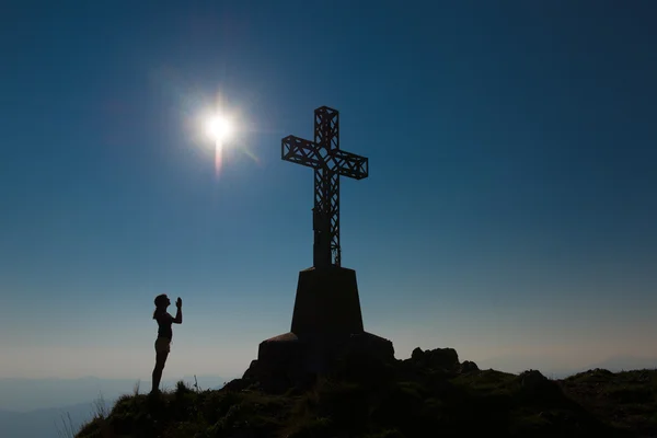 Chica reza en frente de la montaña a la cruz de la cumbre — Foto de Stock