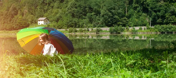 Ребенок играет с цветным зонтиком рядом с озером — стоковое фото