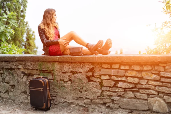Mädchen in der Sonne an einer Wand mit Koffer wartet. — Stockfoto