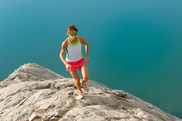 Skyrunner 少女は湖の上石の背部で実行します。 — ストック写真