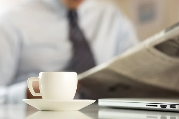 Tasse Kaffee mit Geschäftsmann, der im Hintergrund Zeitung liest — Stockfoto