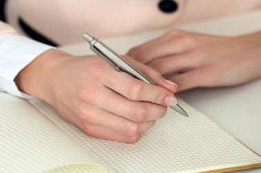 Woman hand holding silver pen ready to make note in opened noteb clipart