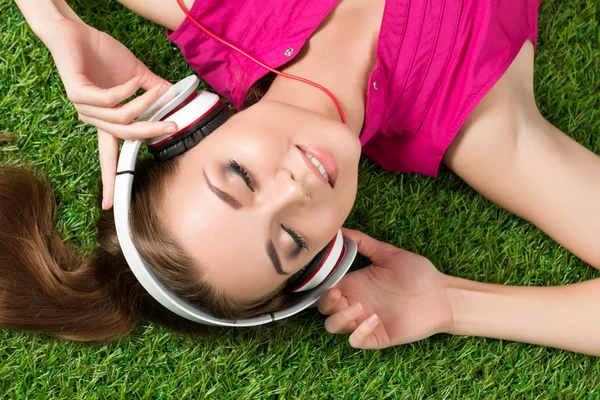 Joven sonriente hermosa chica tendida en la hierba en el parque escuchar —  Fotos de Stock