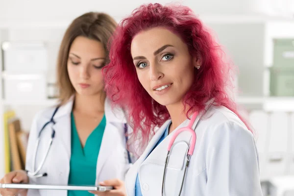 Portrait of two female doctors standing with clipboard and table — Stock Photo, Image