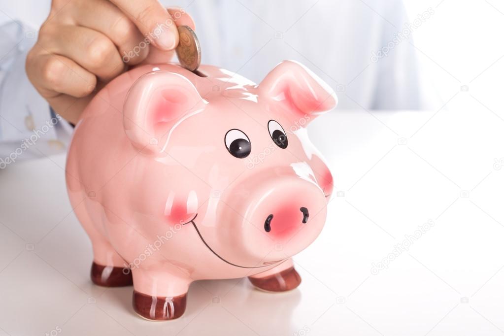 Man's hand putting coin into piggy bank