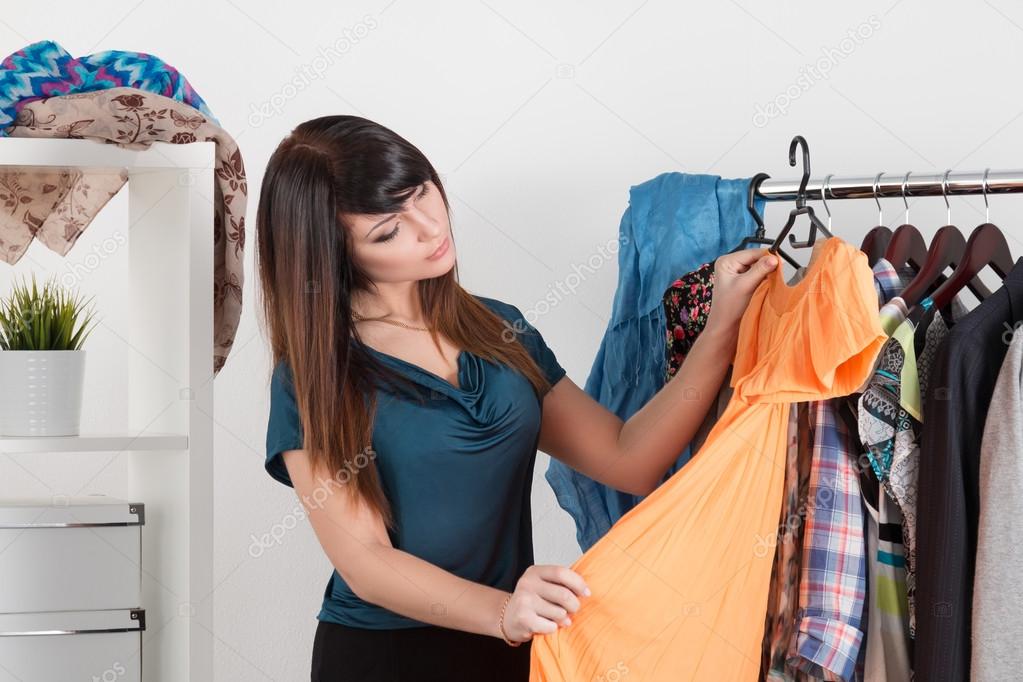 Beautiful young woman near rack with clothes