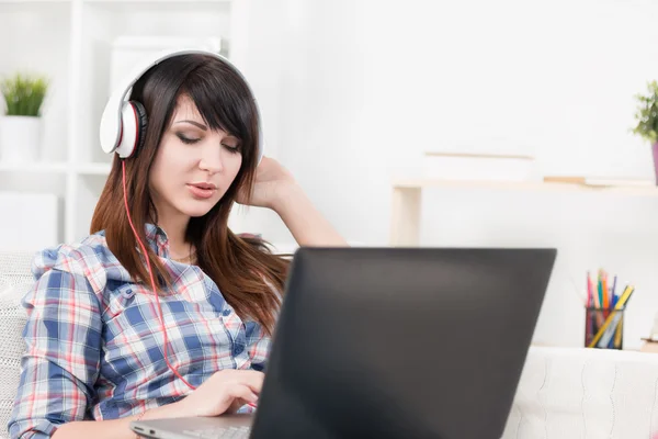 Ganska ung brunett lyssnar musik och skriva in laptop — Stockfoto