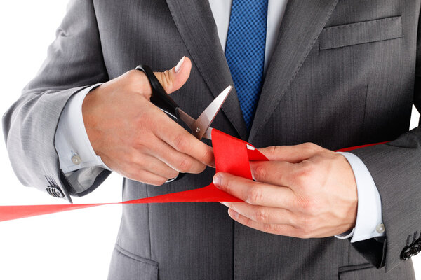 Businessman in suit cutting red ribbon with pair of scissors iso