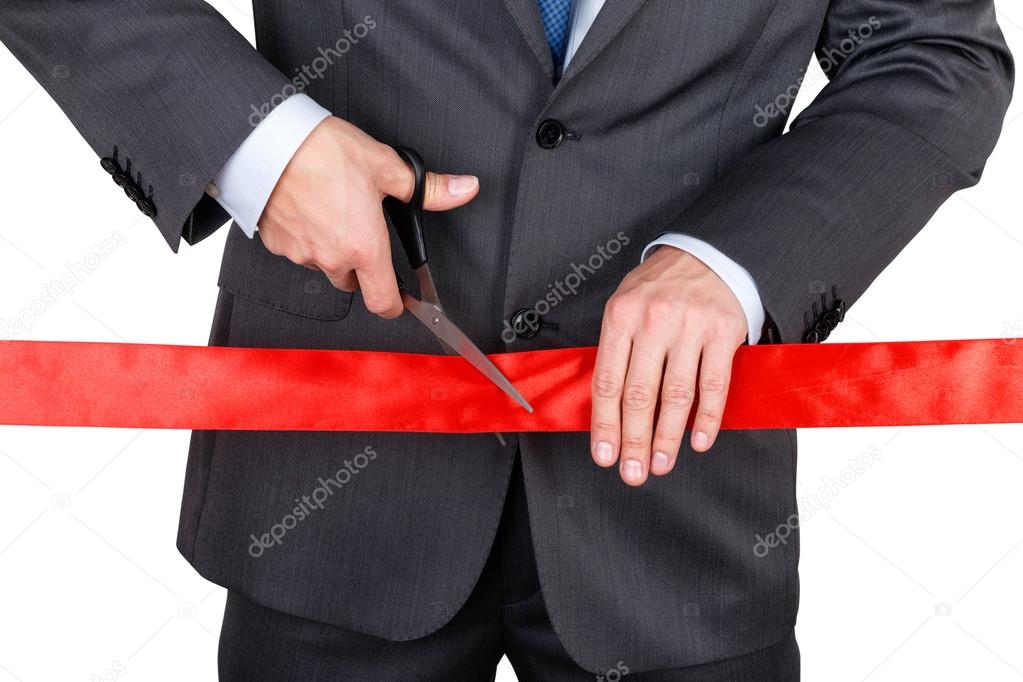 Businessman in suit cutting red ribbon with pair of scissors iso