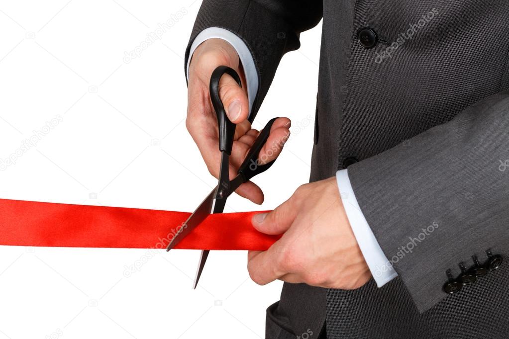 Businessman in suit cutting red ribbon with pair of scissors iso