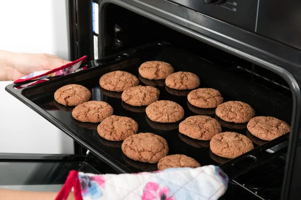 Woman getting roasting pan with oat cookies out of oven — Stock Photo, Image