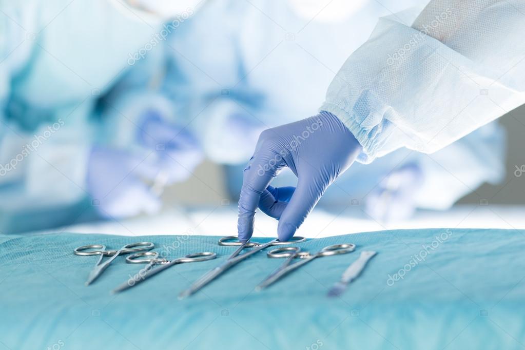 Close-up of scrub nurse taking medical instruments 