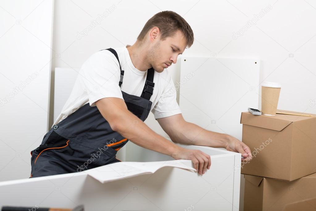 Man dressed in workers' overall assembing furniture