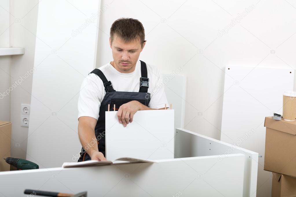 Man dressed in workers' overall assembing furniture